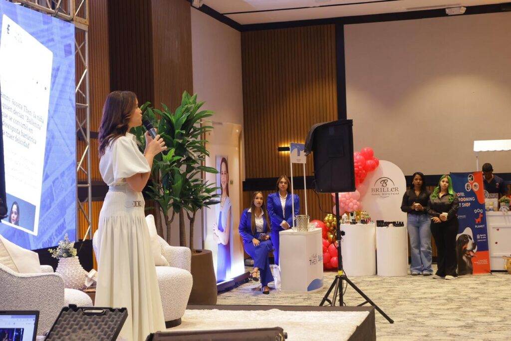 Mujer hablando en evento empresarial con público atento.