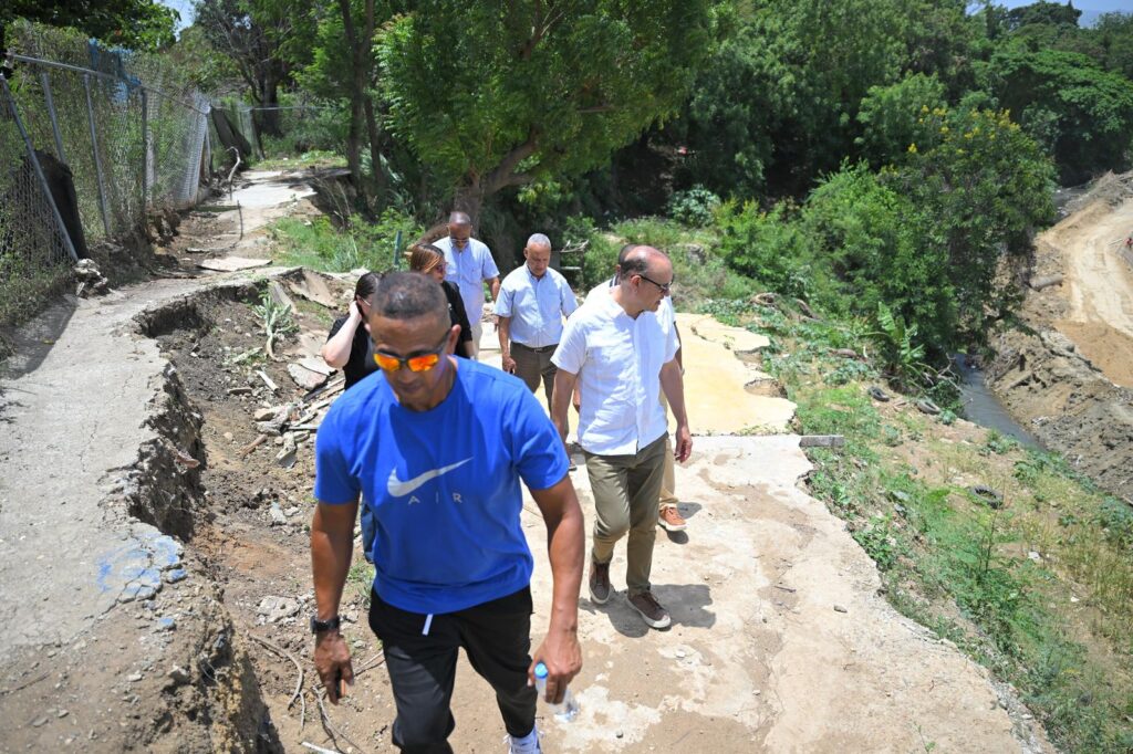 Personas caminando por sendero erosionado en área verde.