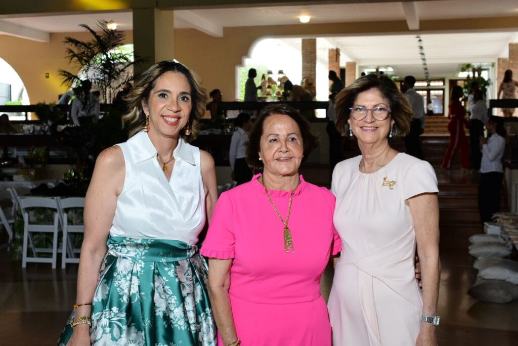 Tres mujeres sonríen en un evento interior elegante.
