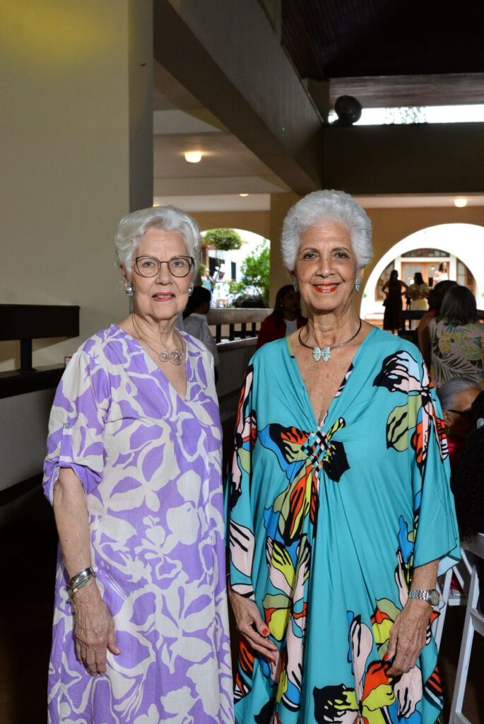 Dos mujeres mayores sonriendo en interior con túnicas coloridas.