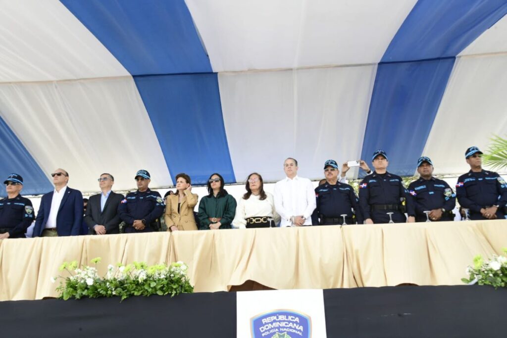 Funcionarios en evento bajo carpa azul y blanca.