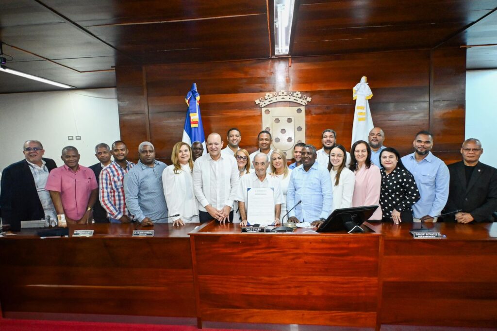 Grupo de personas en un salón oficial con banderas.