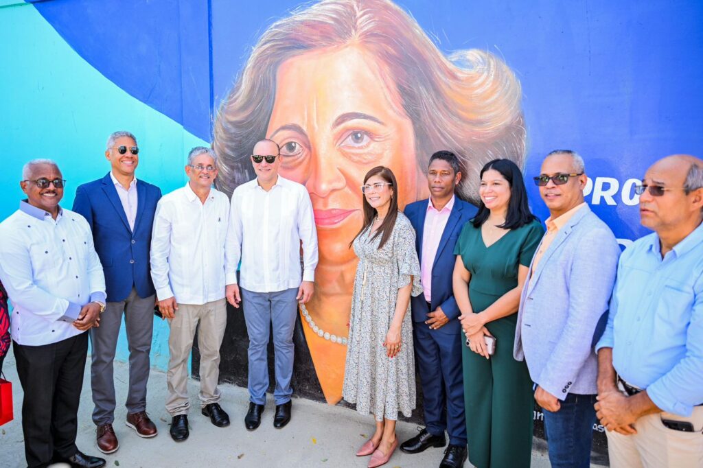 Personas posan frente a un mural femenino colorido.