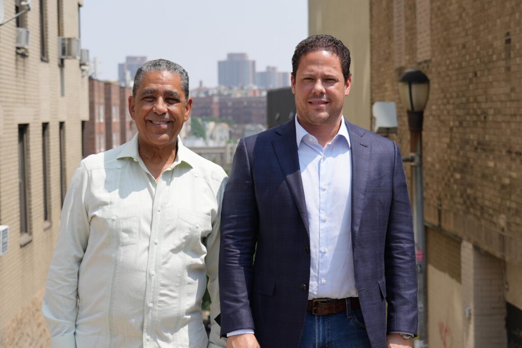 Dos hombres posando en una calle urbana soleada.