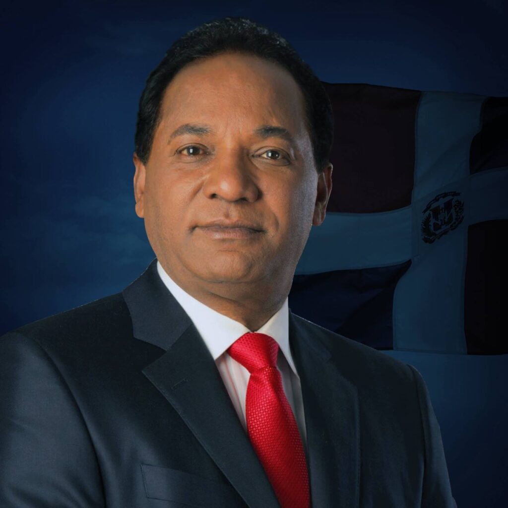 Hombre con traje frente a bandera dominicana.