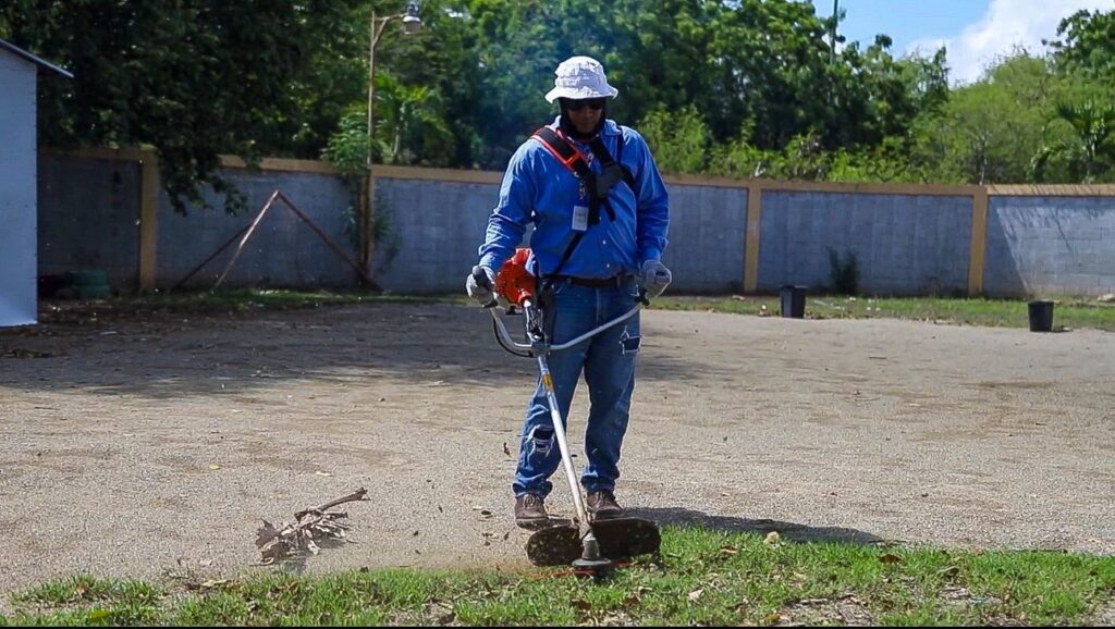 Hombre cortando césped con desbrozadora en el jardín.