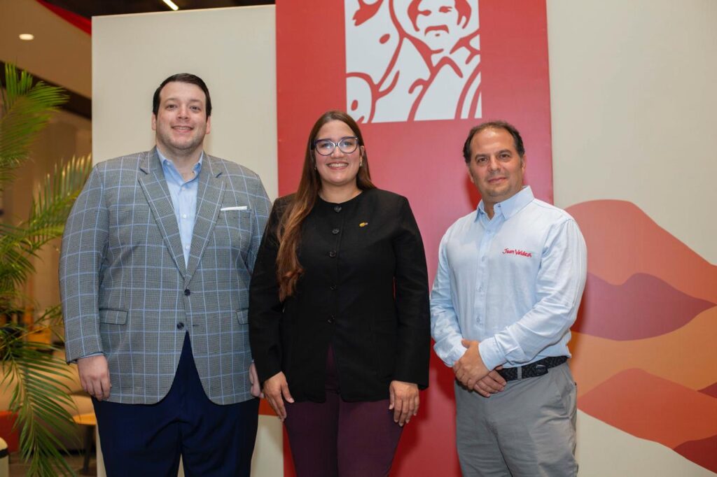 Tres personas posan frente a mural rojo.