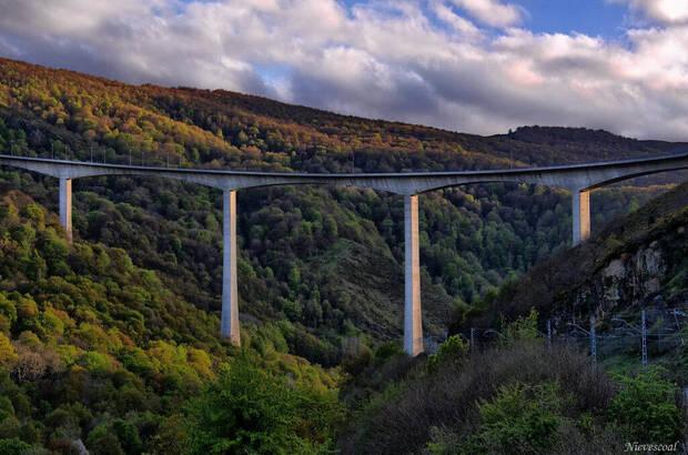 Viaducto sobre un valle boscoso y montañas.