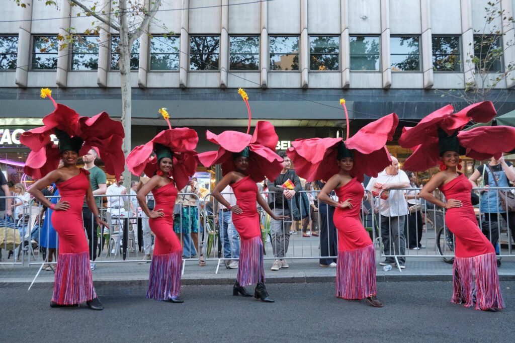 Bailarinas con trajes florales rojos en desfile urbano.