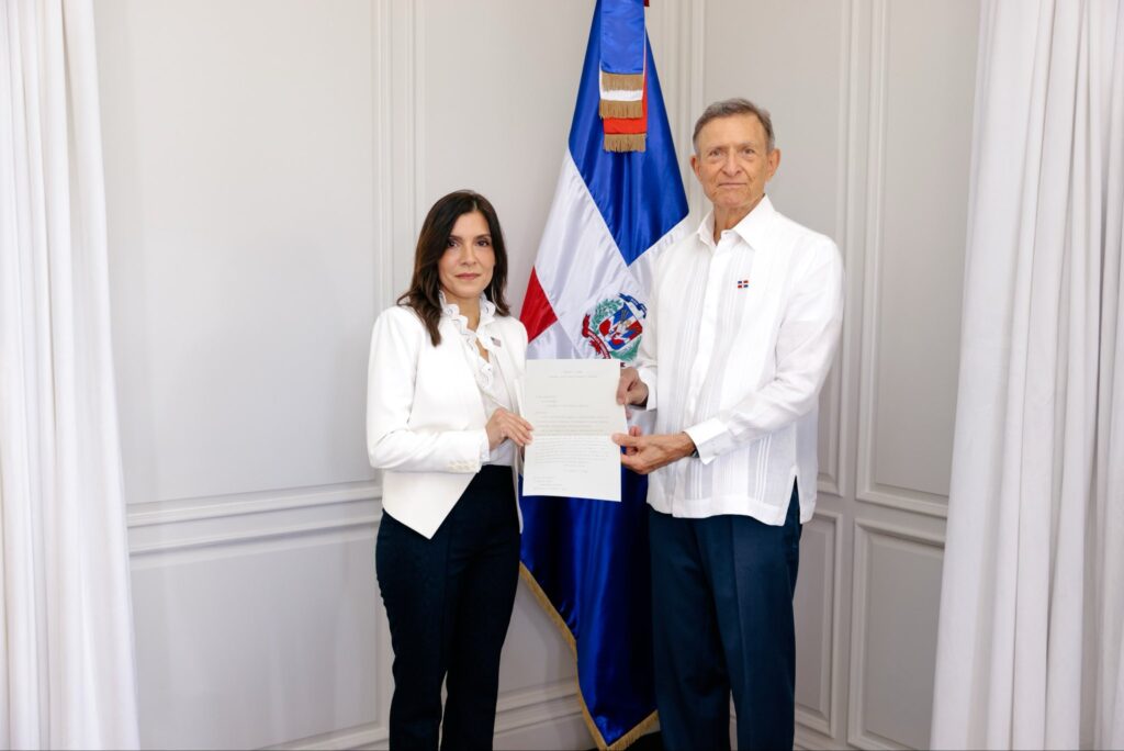 Entrega de documento oficial junto a bandera dominicana.