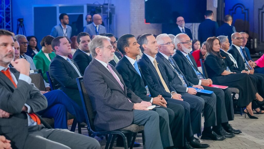 Personas en conferencia pública vistiendo trajes formales.