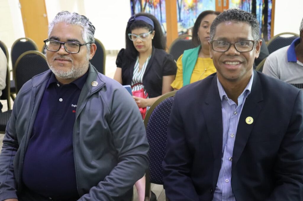 Hombres sonriendo en un evento público, personas detrás