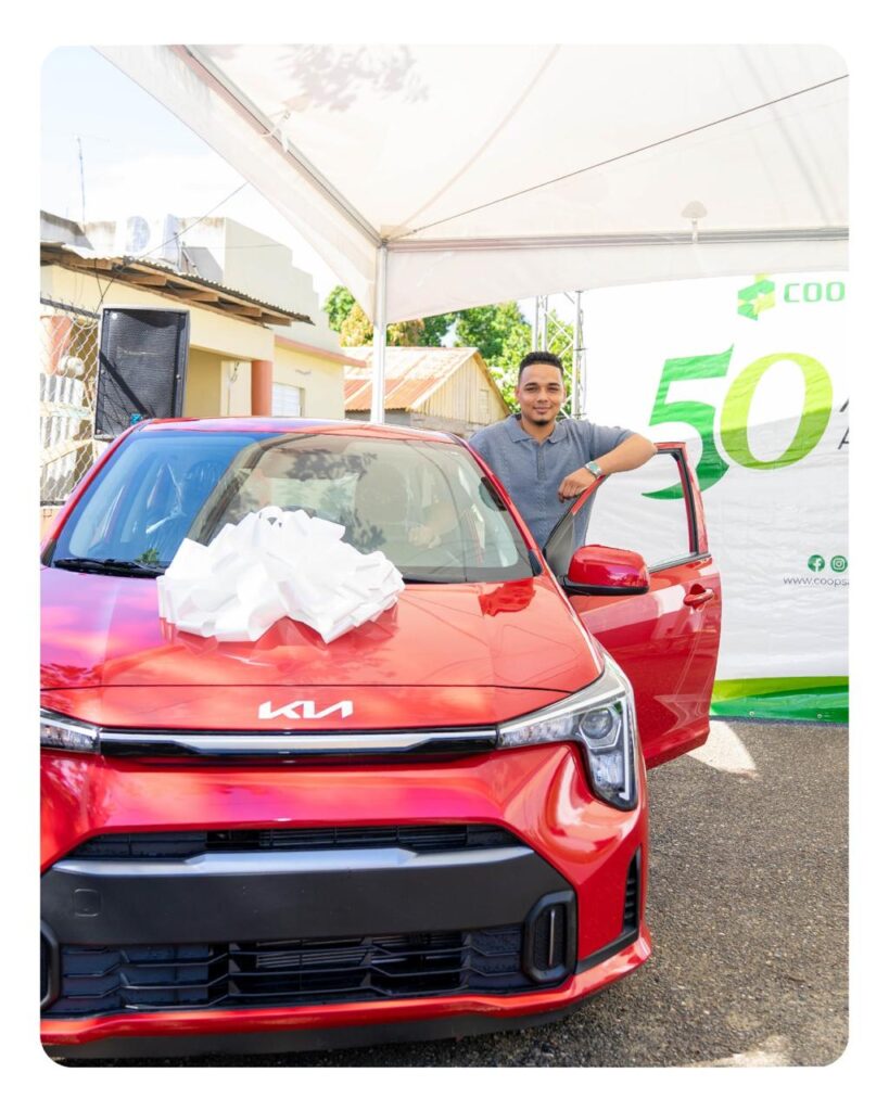 Hombre junto a coche nuevo rojo con lazo blanco.