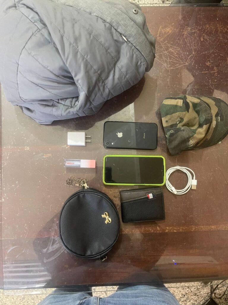 Objetos personales sobre mesa: ropa, teléfonos, cargador.