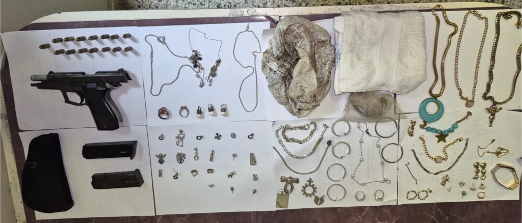 Arma, municiones y joyería sobre mesa blanca.