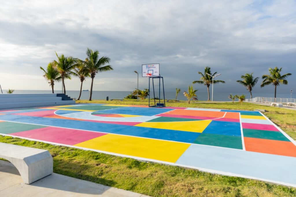 Cancha de baloncesto colorida junto al mar y palmeras.