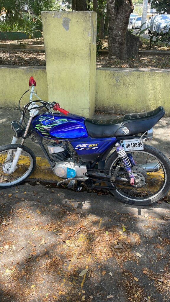 Motocicleta azul estacionada en una acera sombreada.