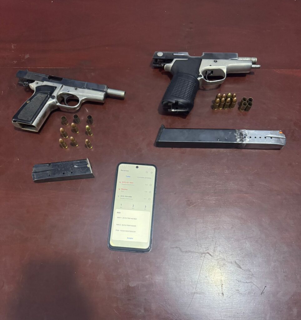 Dos pistolas, municiones y teléfono sobre mesa marrón.
