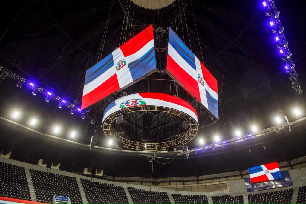 Pantallas con bandera dominicana en estadio cubierto.