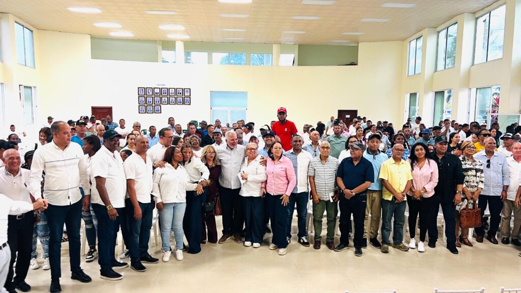 Reunión grupal en salón con muchas personas reunidas.