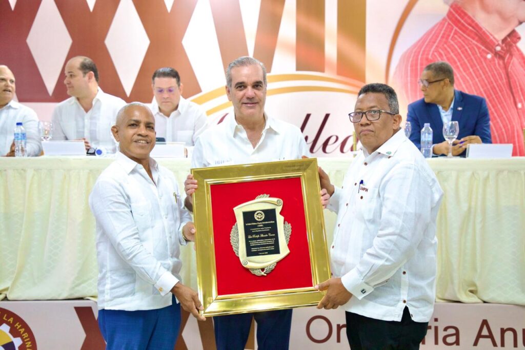 Hombres entregan placa de reconocimiento en evento formal.