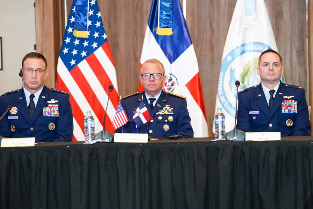 Oficiales militares en conferencia con banderas de fondo.