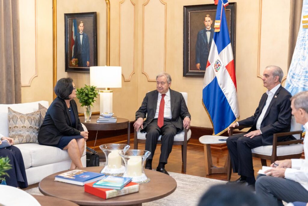 Reunión oficial en sala con banderas y retratos.