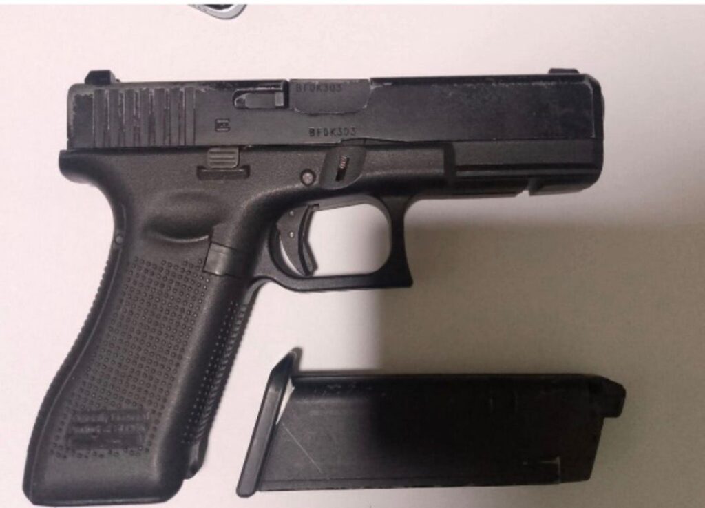 Pistola semiautomática con cargador vacío en mesa blanca.
