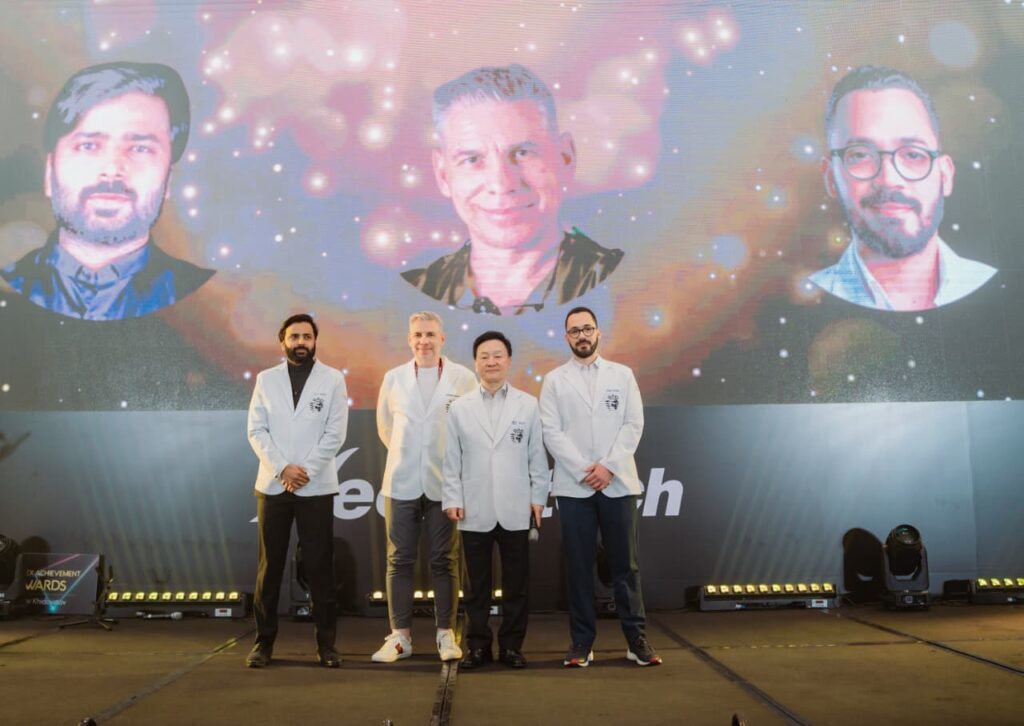 Grupo de hombres en evento con proyecciones en pantalla.