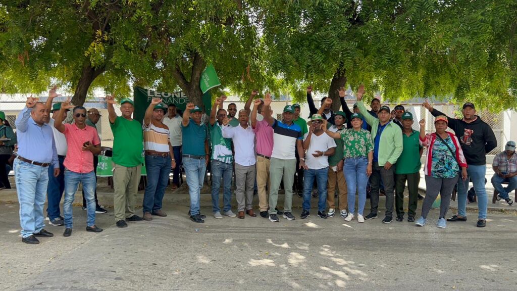 Personas reunidas bajo un árbol con banderas verdes.