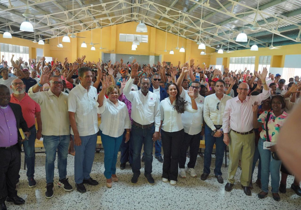 Reunión comunitaria con muchas personas levantando la mano.